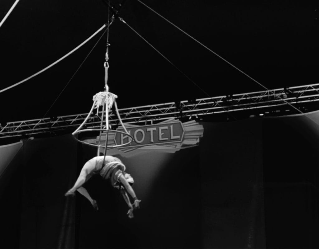 Black and white photo of a woman hanging from an aerial hoop.