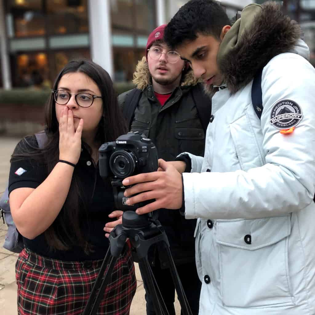 Three young people filming on a camera.