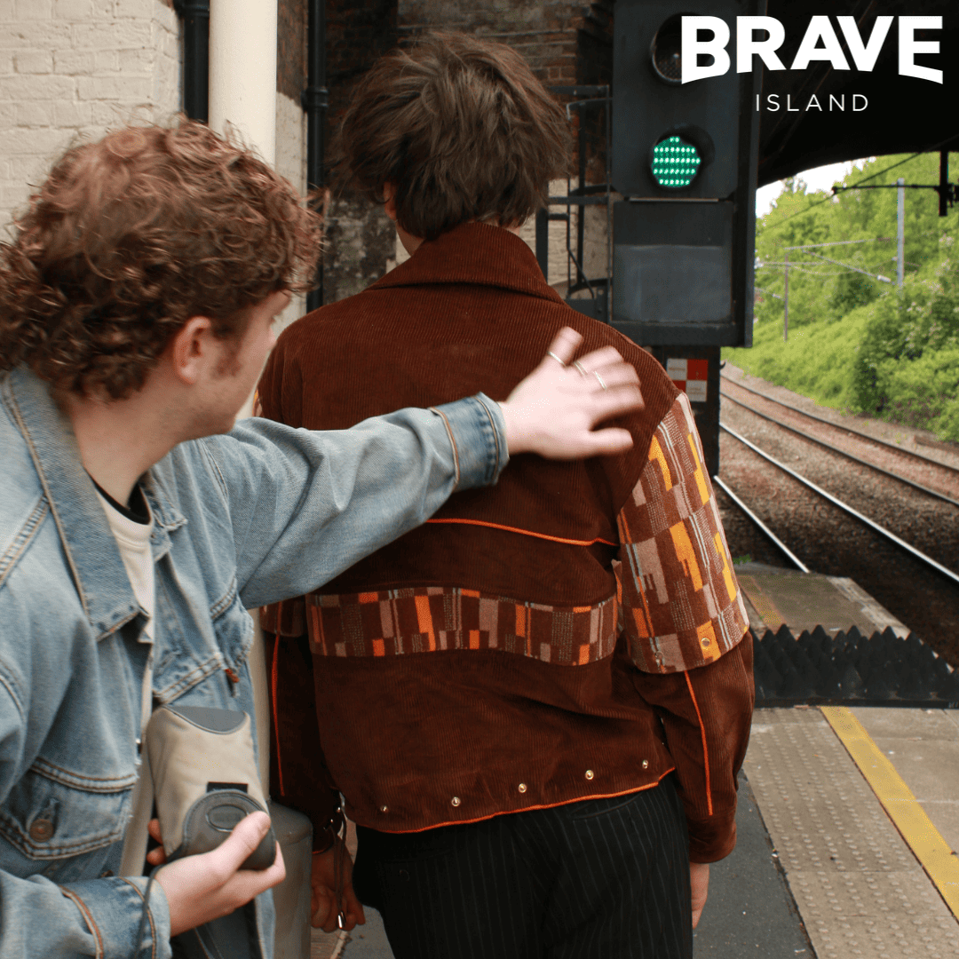 Two people facing away from the camera and standing on the platform at a train station