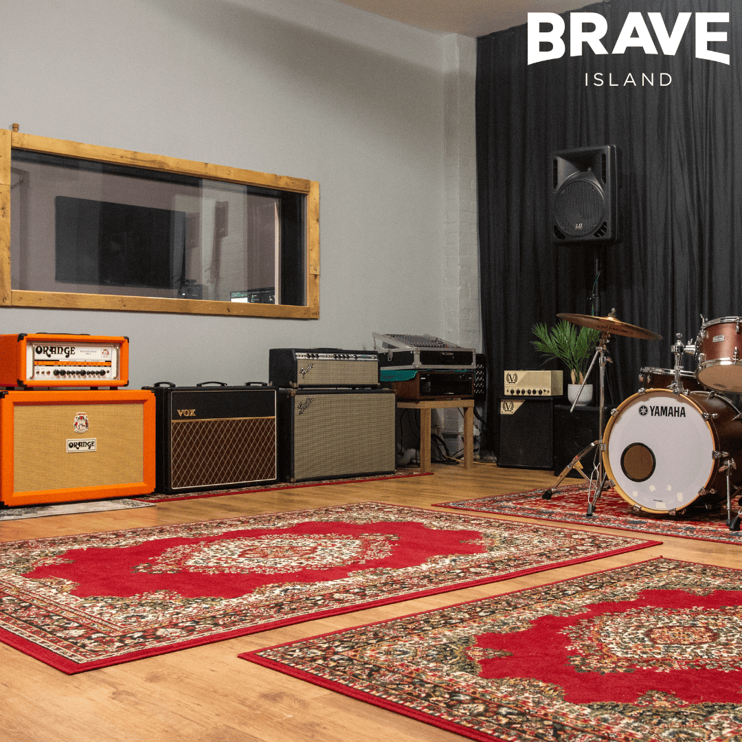 Image of a recording studio with a drum kit, amps, and rugs on the floor.