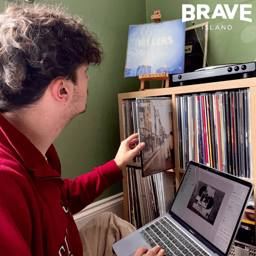 a man looks through a vinyl record collection whilst designing an image on his laptop