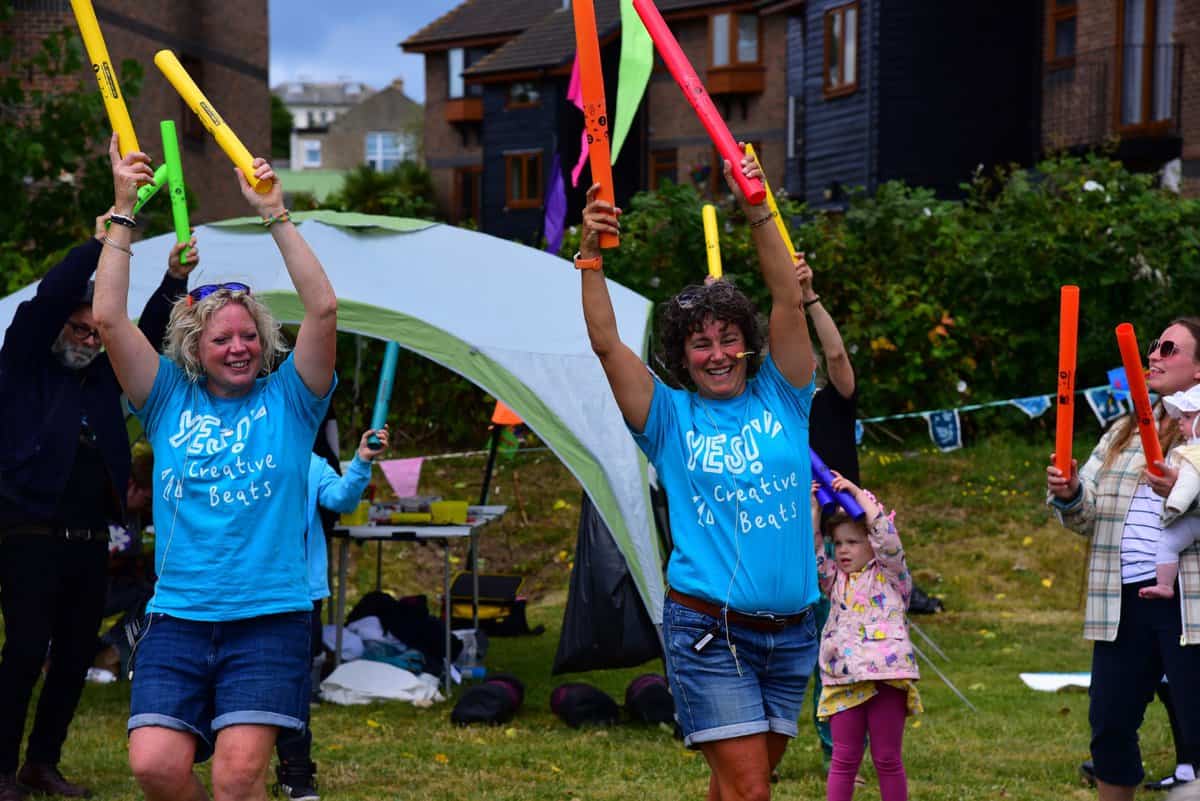 Two ladies in baby blue t-shirts. They are holding Boom Whackers (plastic tubes for making music) above their heads