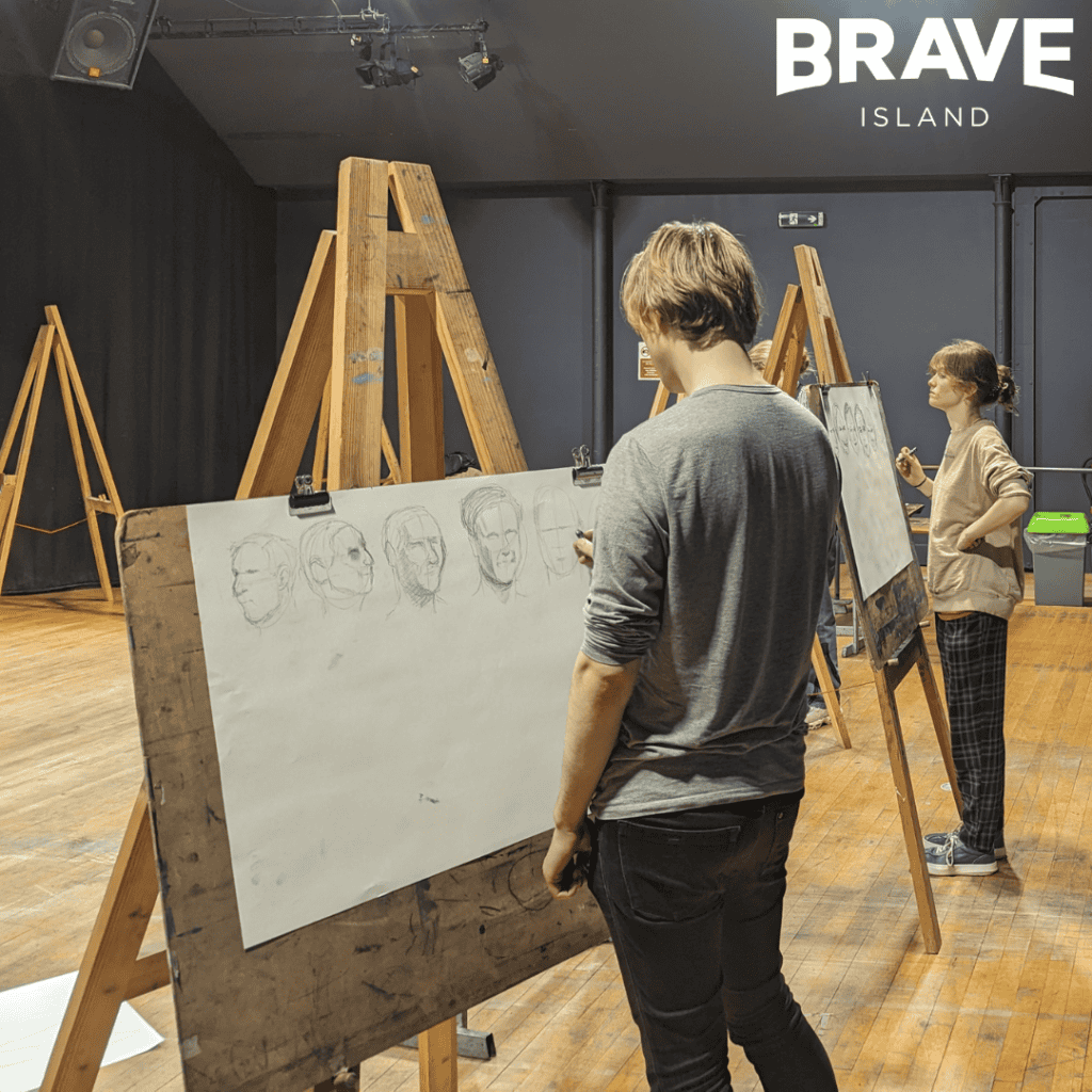 Two figures standing at easels. They are drawing faces with Charcoal as part of a Life Drawing workshop