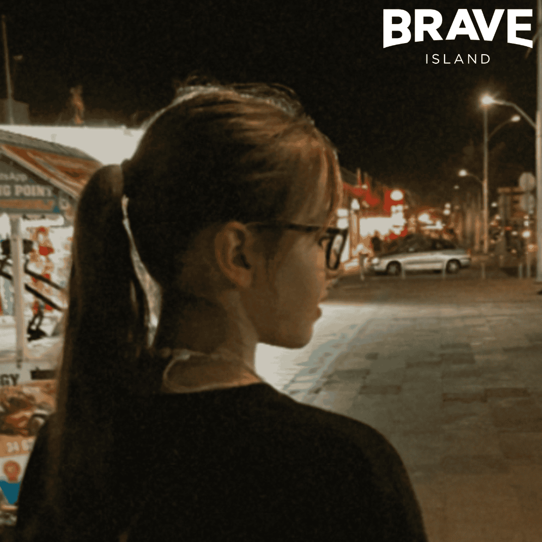 A young person with a ponytail facing away from the camera looking right. She's standing outside at night