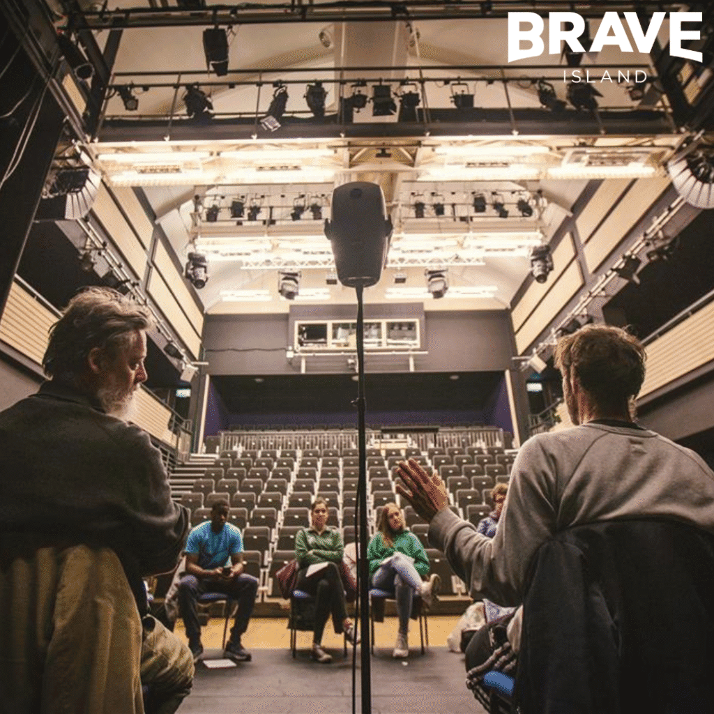 A workshop taking place in a small-medium sized theatre. All participants are seated on stage around a binaural microphone in the shape of a humanoid head.