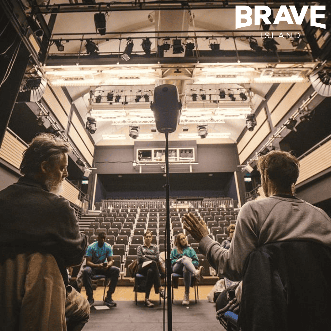 A workshop taking place in a small-medium sized theatre. All participants are seated on stage around a binaural microphone in the shape of a humanoid head.