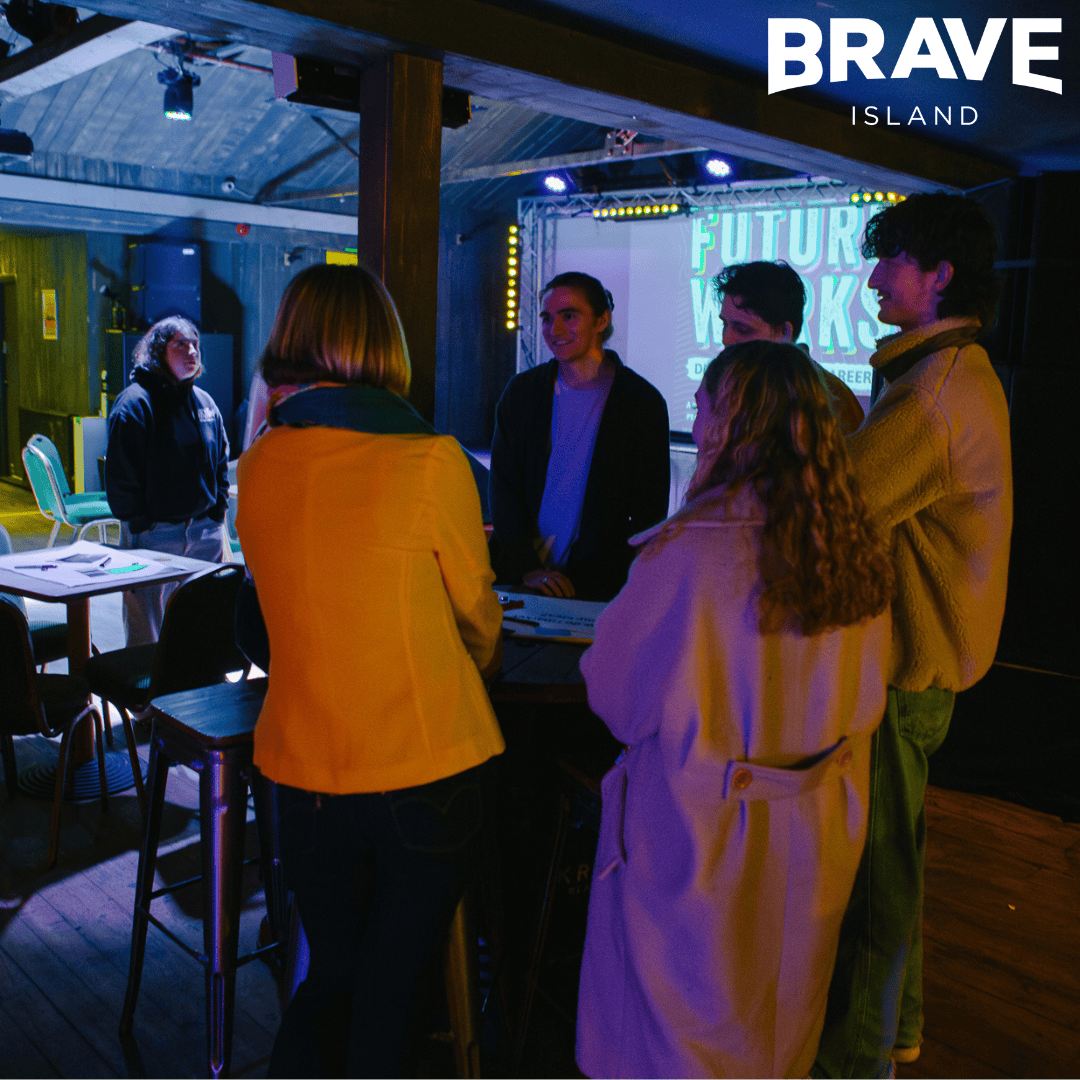 A group of people stood around a table, chatting in a dimly lit room.