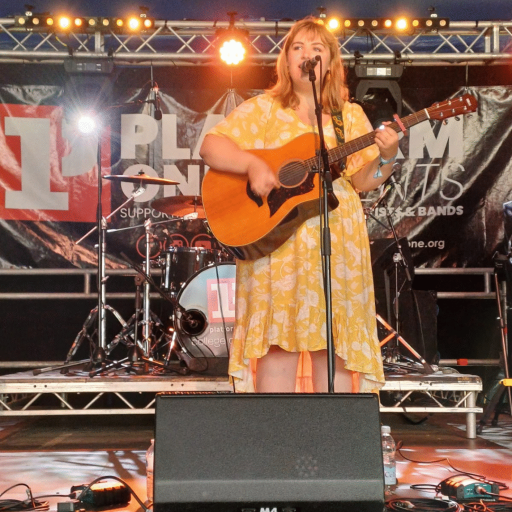 Singer-Songwriter Amy Jolliffe performing with a guitar on the Platform One stage