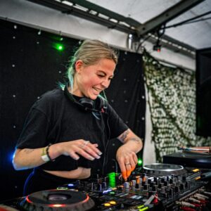 A photograph featuring a DJ at a turntable in a marquee.