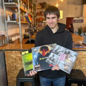 A young man holding up three records in a record shop