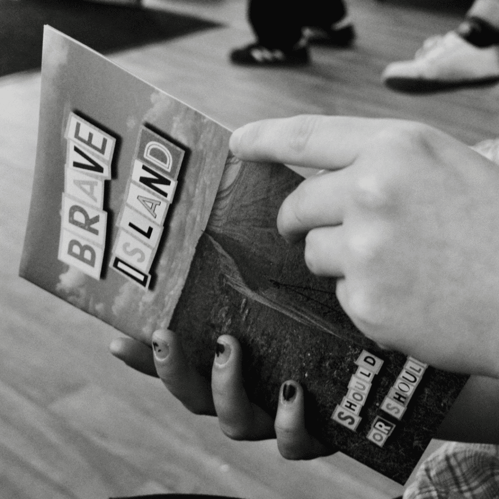 a black and white image of two hands holding a copy of the Brave Island Zine