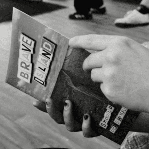 a black and white image of two hands holding a copy of the Brave Island Zine