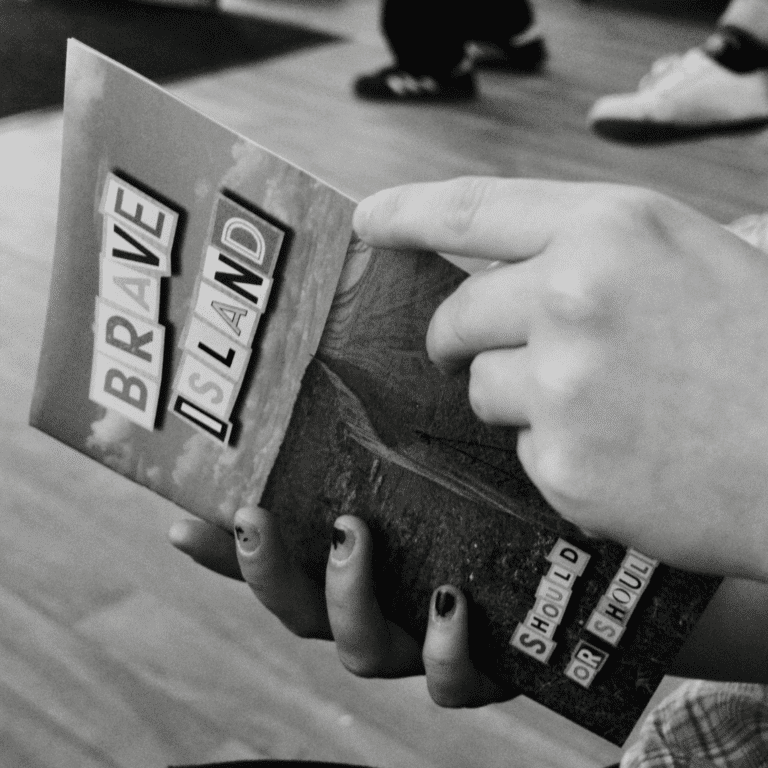 a black and white image of two hands holding a copy of the Brave Island Zine