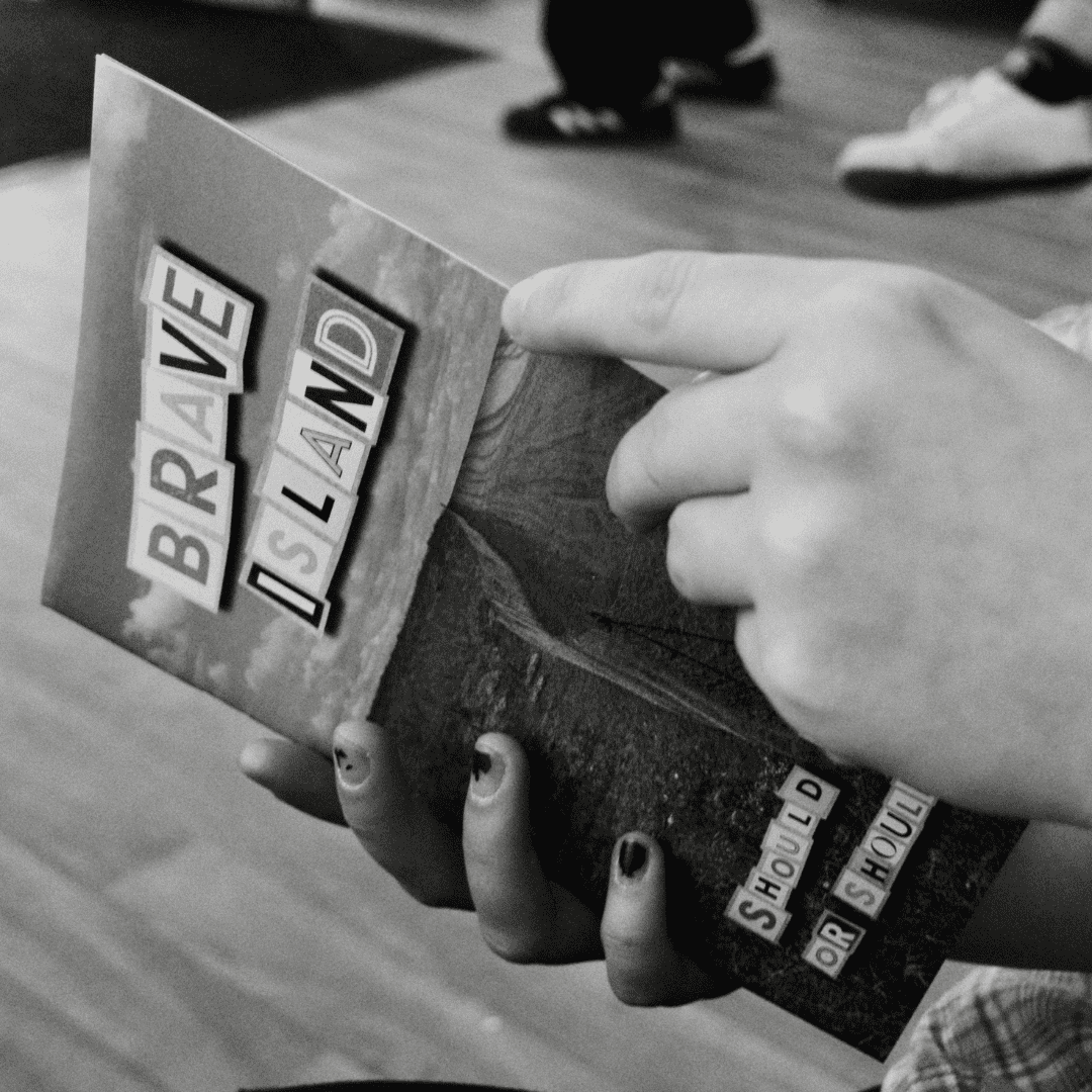 a black and white image of two hands holding a copy of the Brave Island Zine