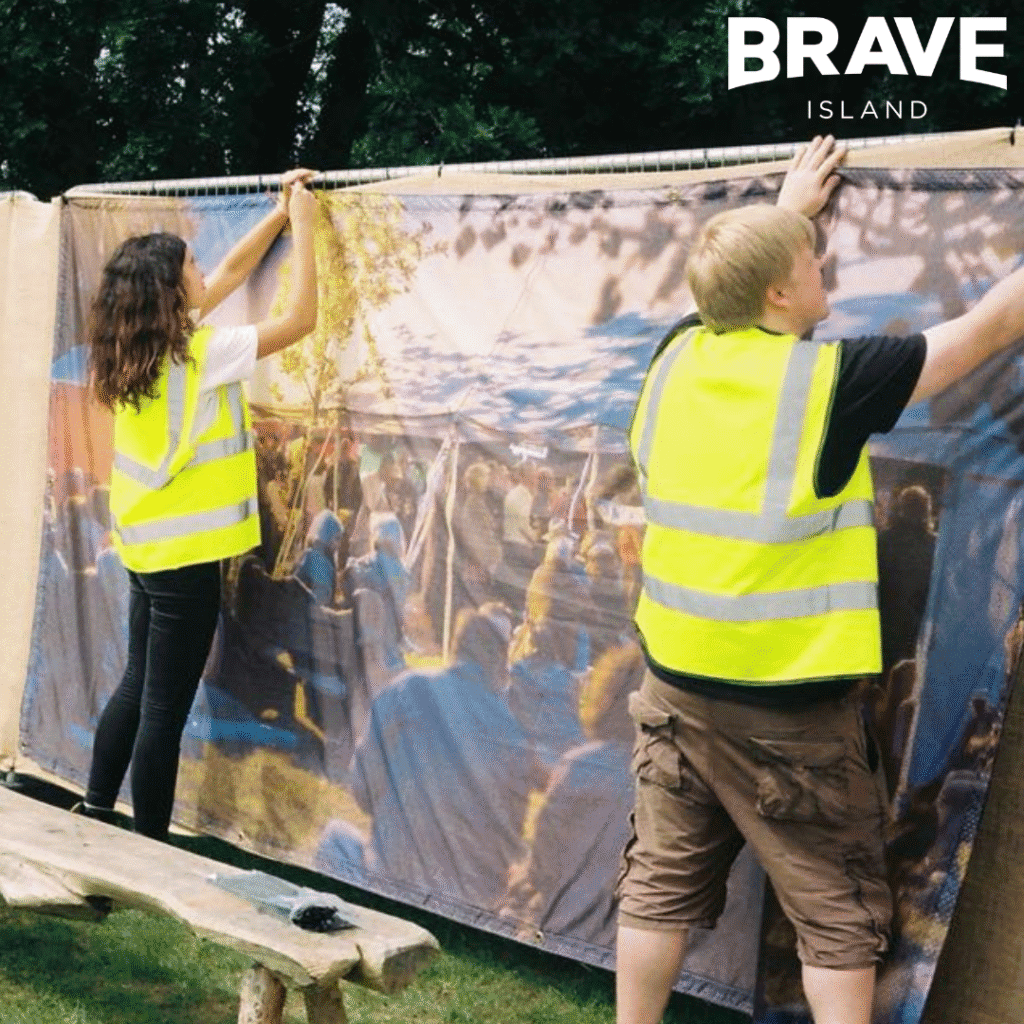 Two festival crew attaching artwork to fencing