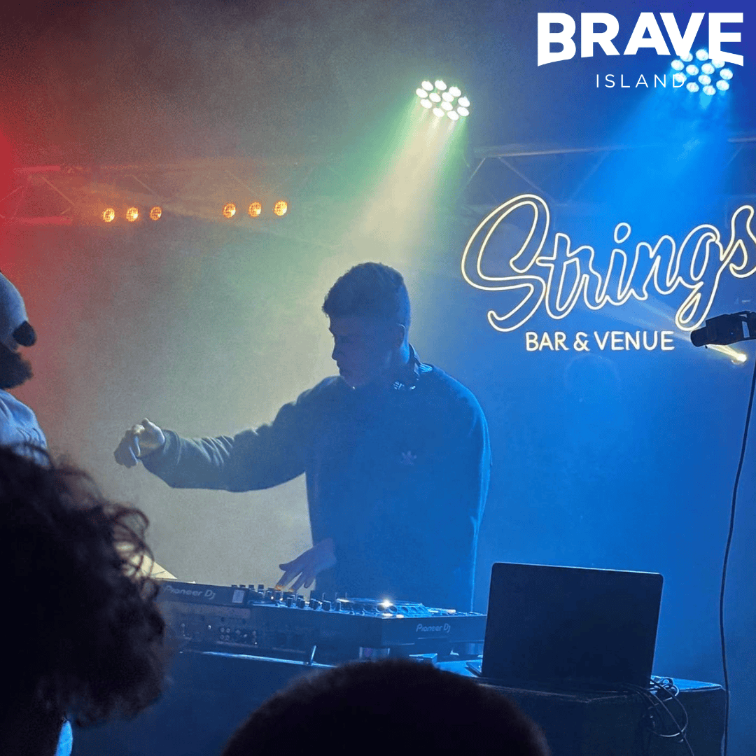 Sonnie, a young man, DJs behind the decks on stage at Strings Bar & Venue