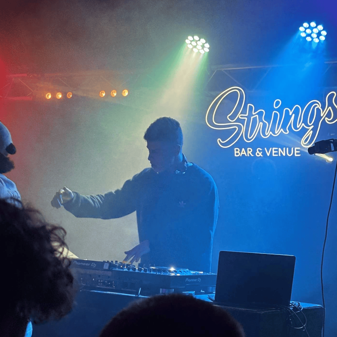 Sonnie, a young man, DJs behind the decks on stage at Strings Bar & Venue