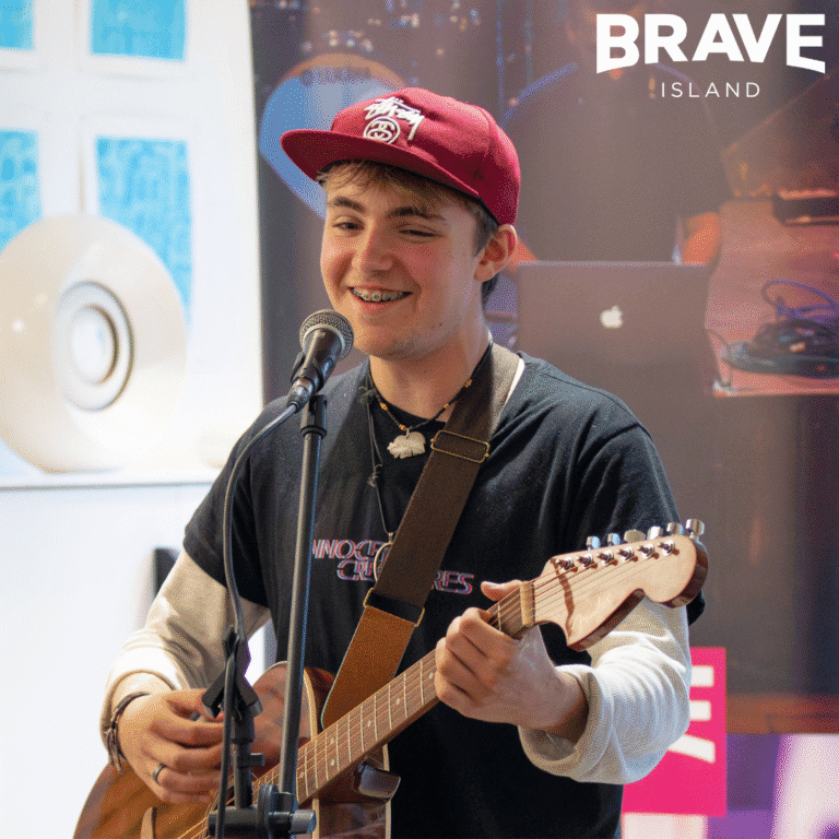 A young man playing guitar and singing into a microphone