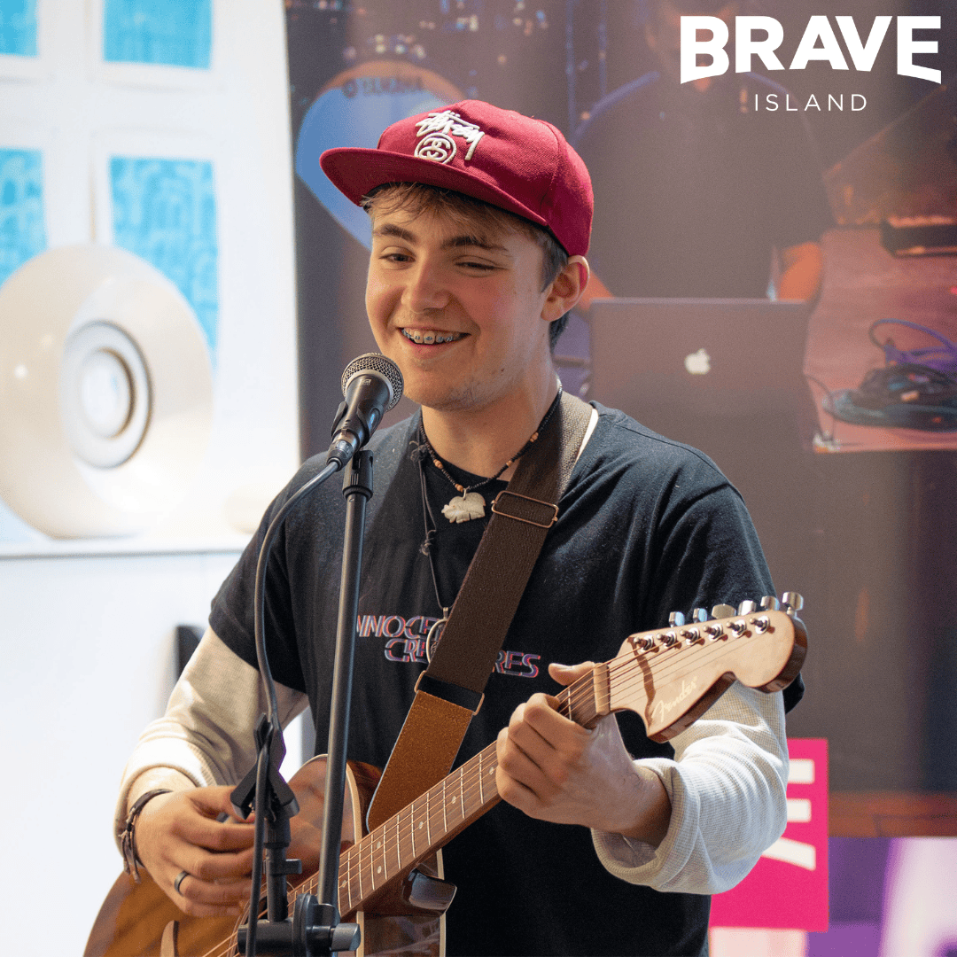 A young man playing guitar and singing into a microphone