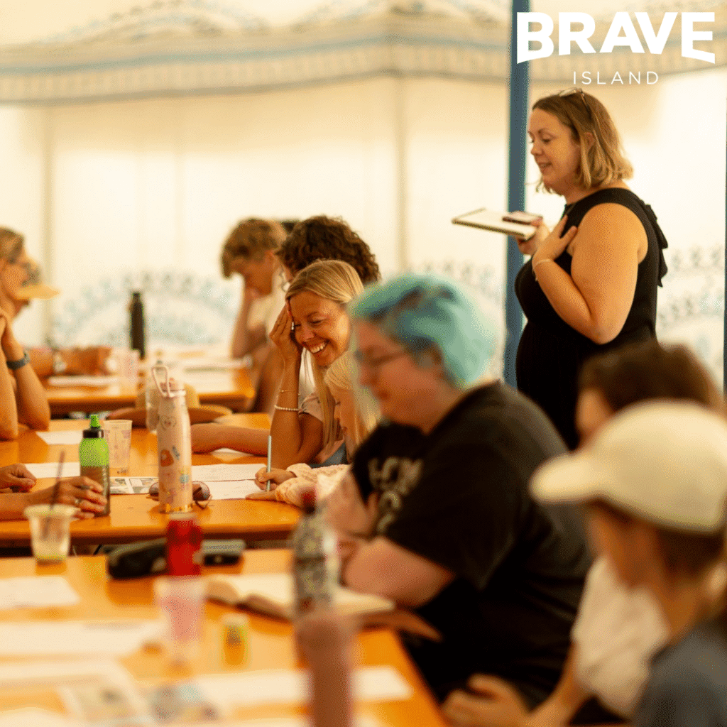 A photograph showing people sat around a line of tables. They are taking part in a drawing workshop at Ventnor Fringe