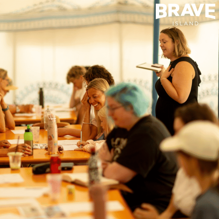 A photograph showing people sat around a line of tables. They are taking part in a drawing workshop at Ventnor Fringe