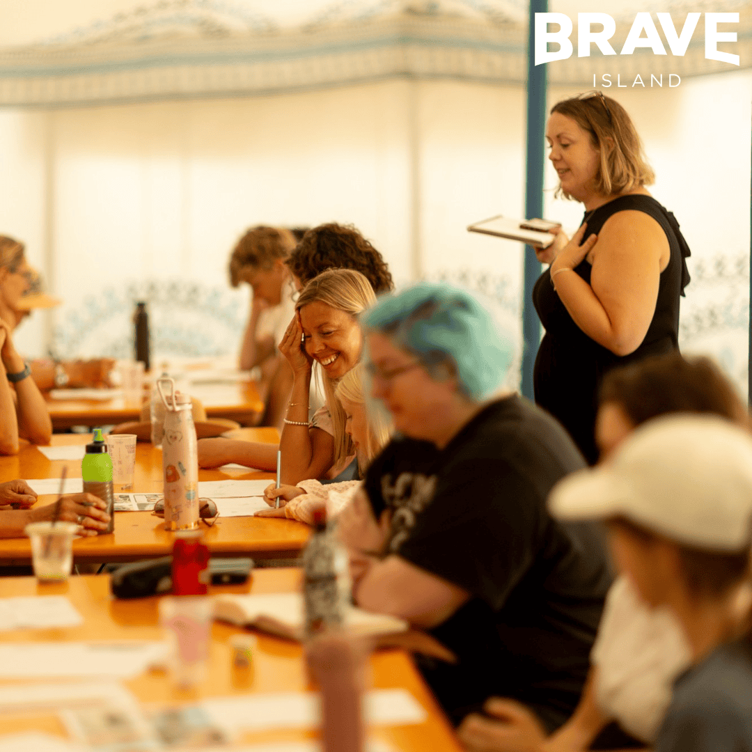 A photograph showing people sat around a line of tables. They are taking part in a drawing workshop at Ventnor Fringe